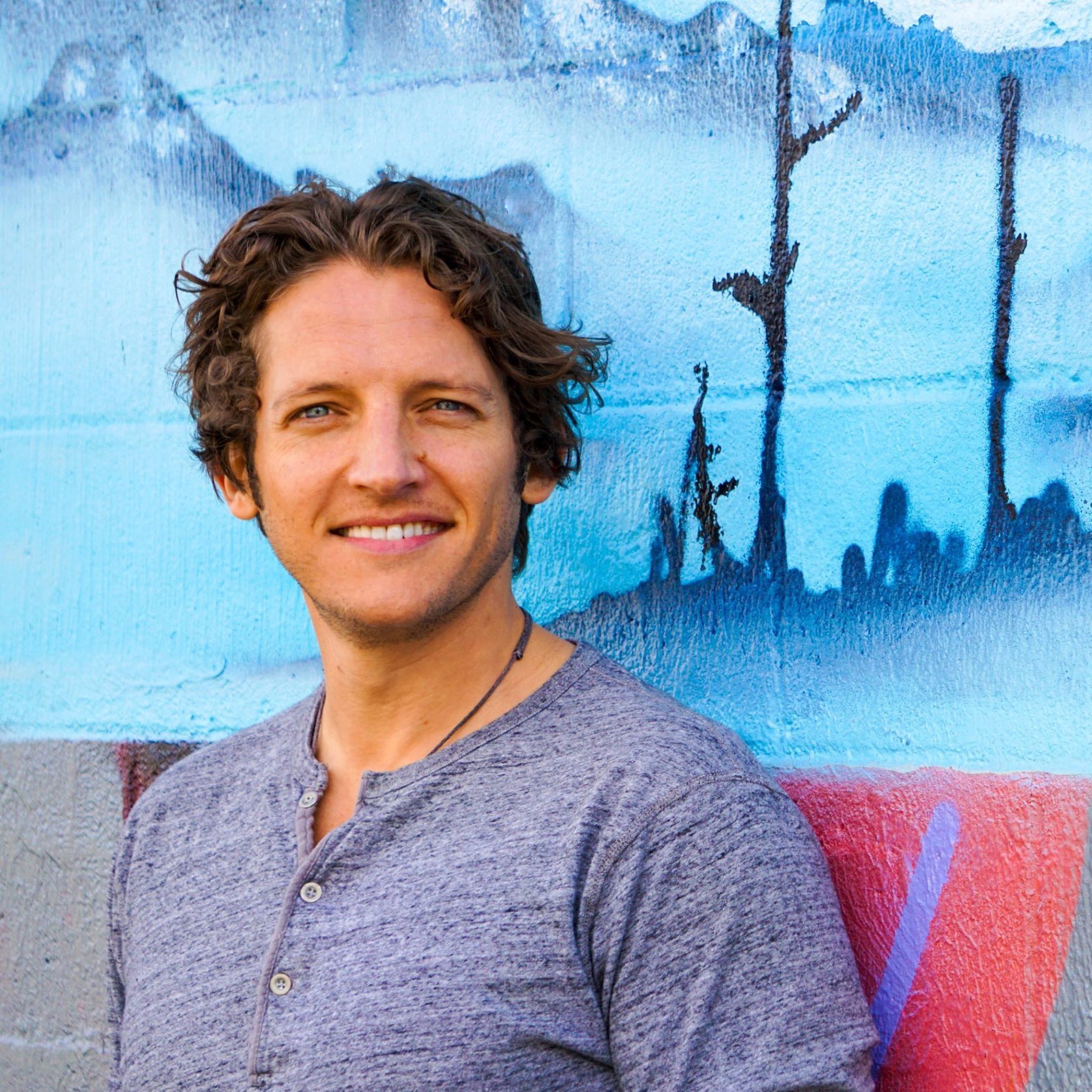 Logan Crowell smiling in front of a blue mural